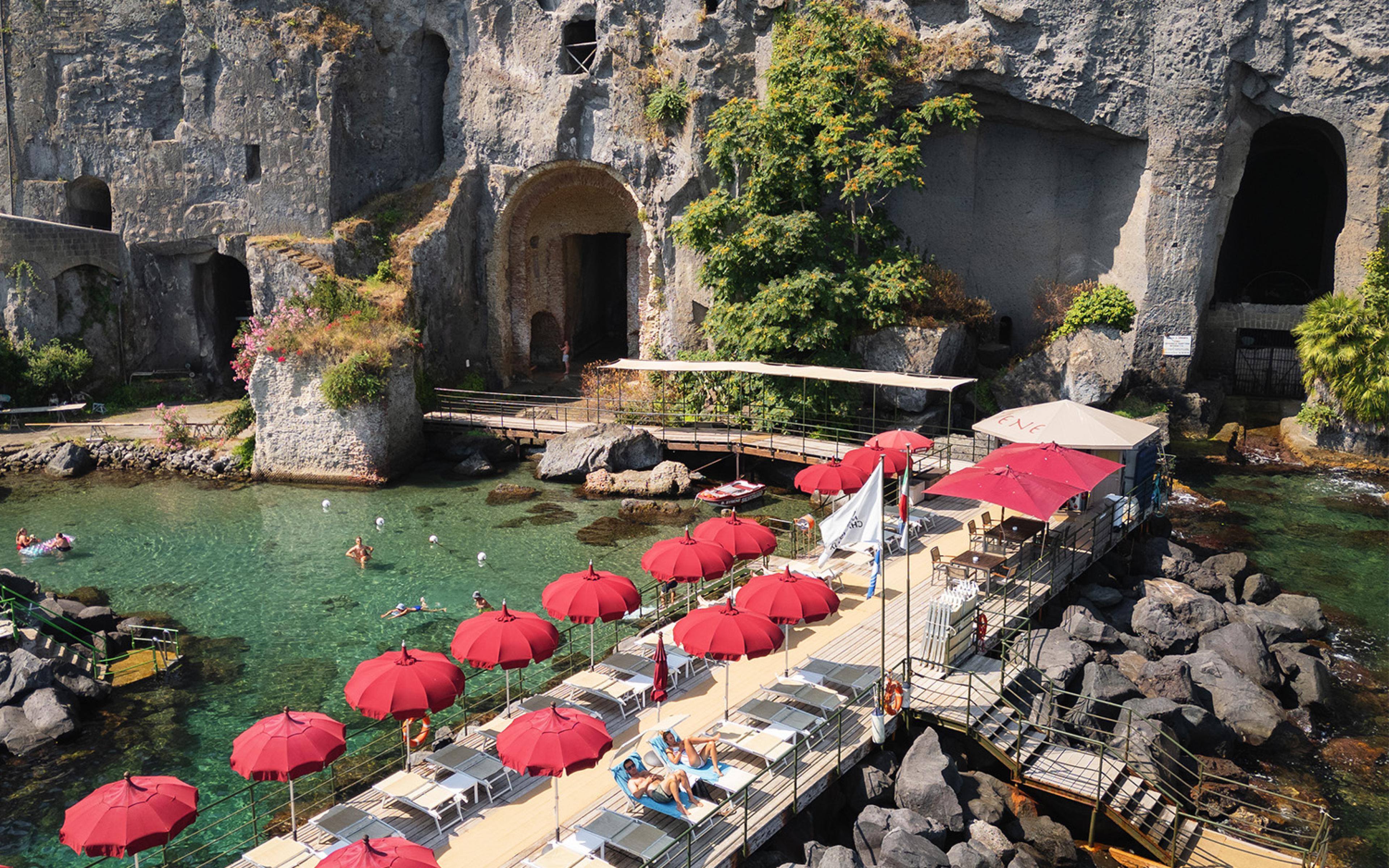 red umbrellas over lounge chairs on a private seaside area, built on a foundation of rocks 
