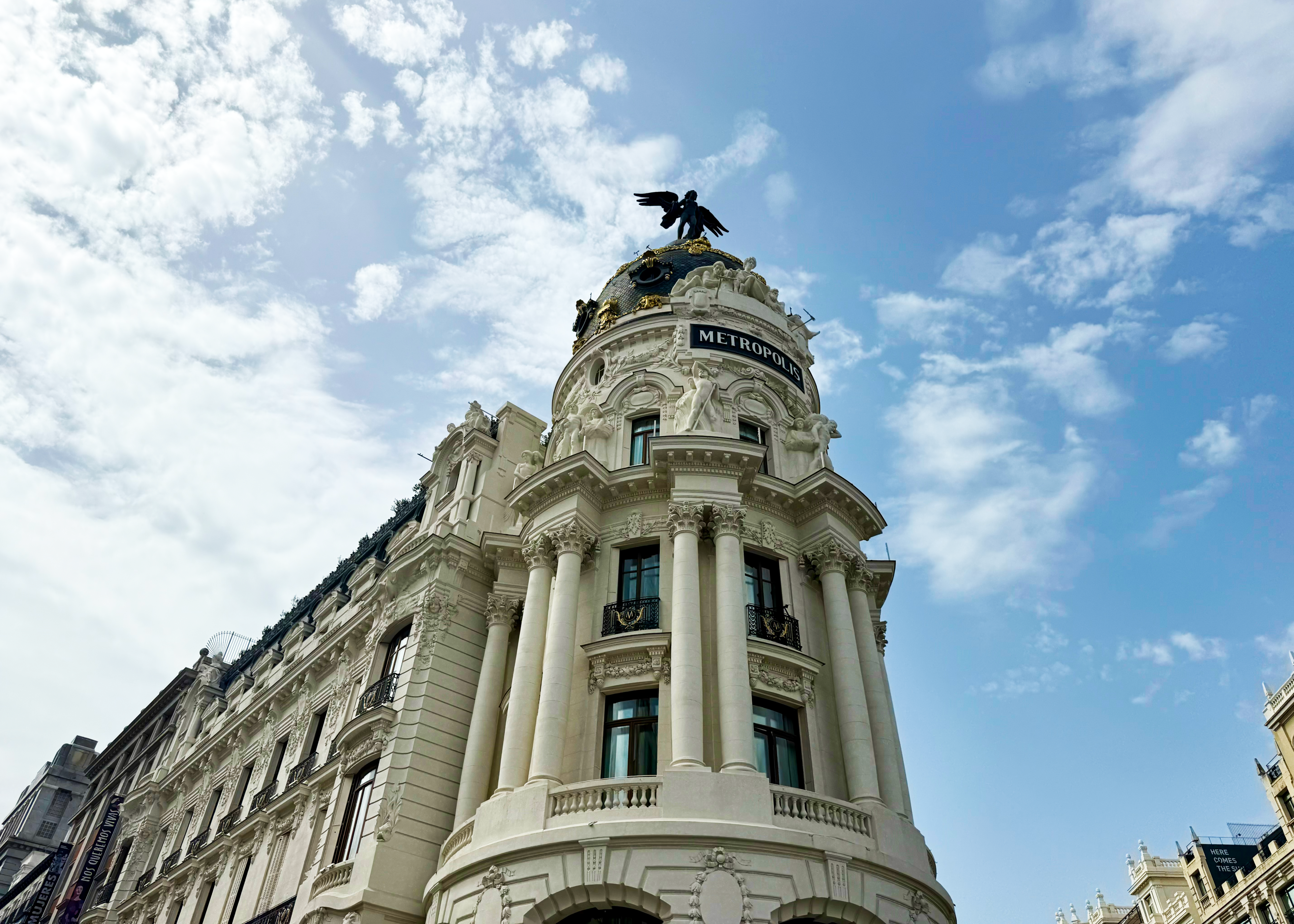 exterior of white baux arts building in madrid with cupola tower with statue on it and sign saying "metropolis" seen from street level