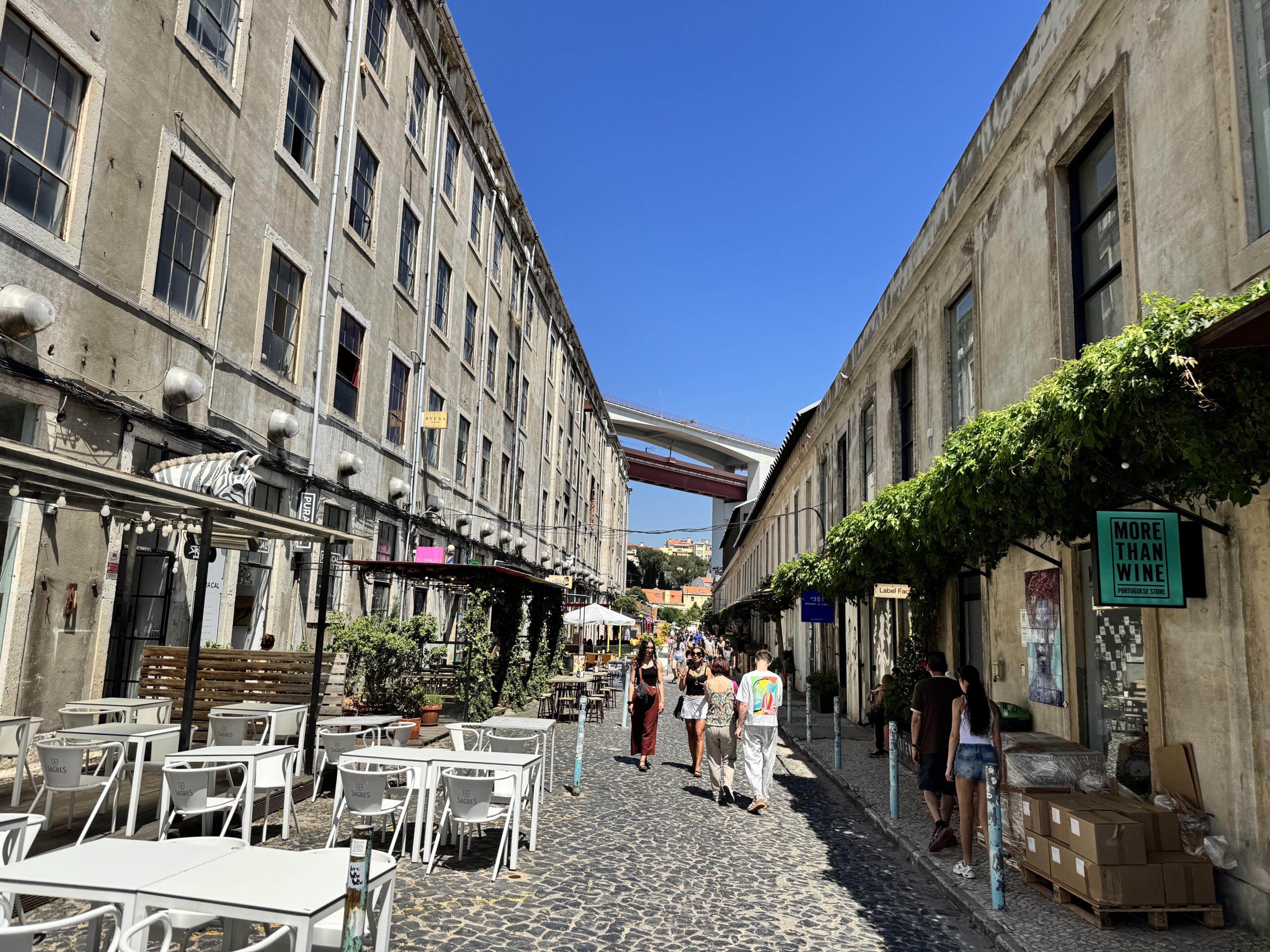 LX Factory in Lisbon seen on sunny day with people walking between shops in old warehouse district
