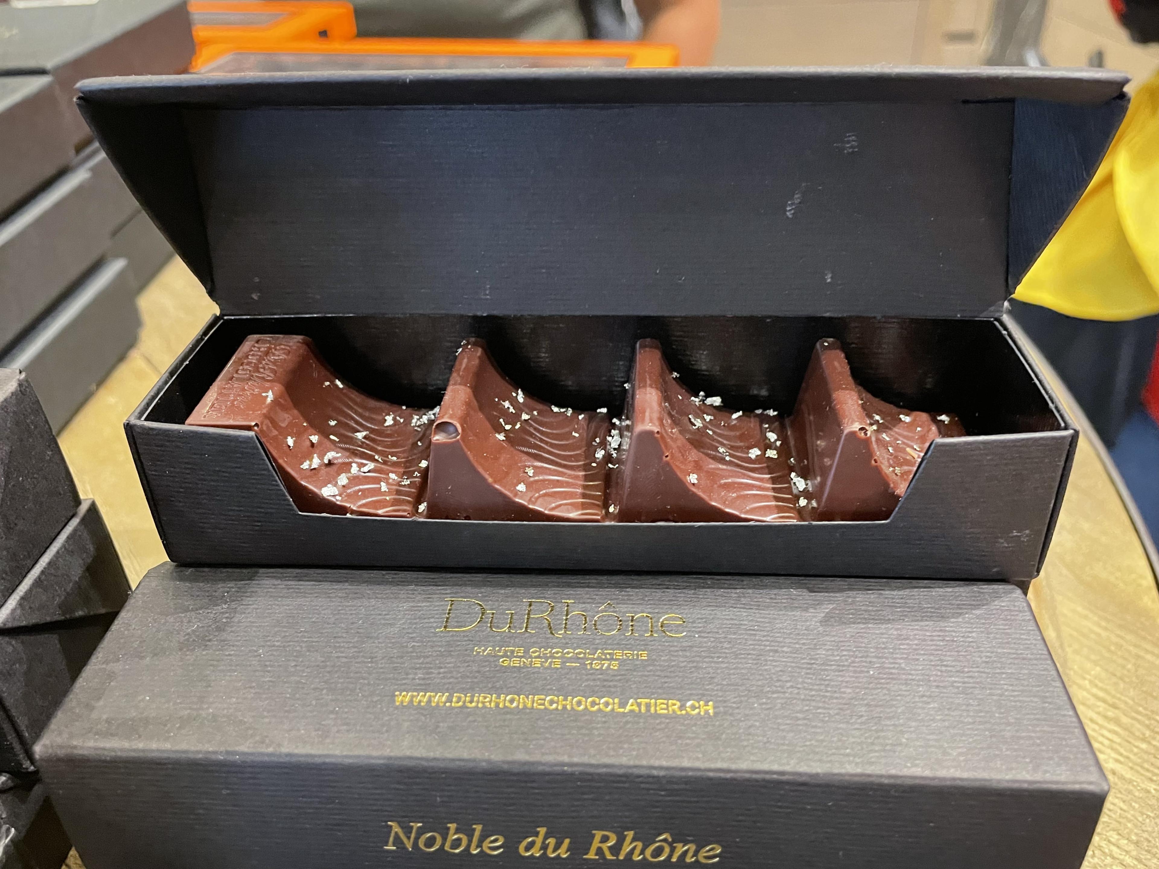 Close-up of DuRhône chocolates in black boxes, topped with silver flakes and gold lettering on the packaging.