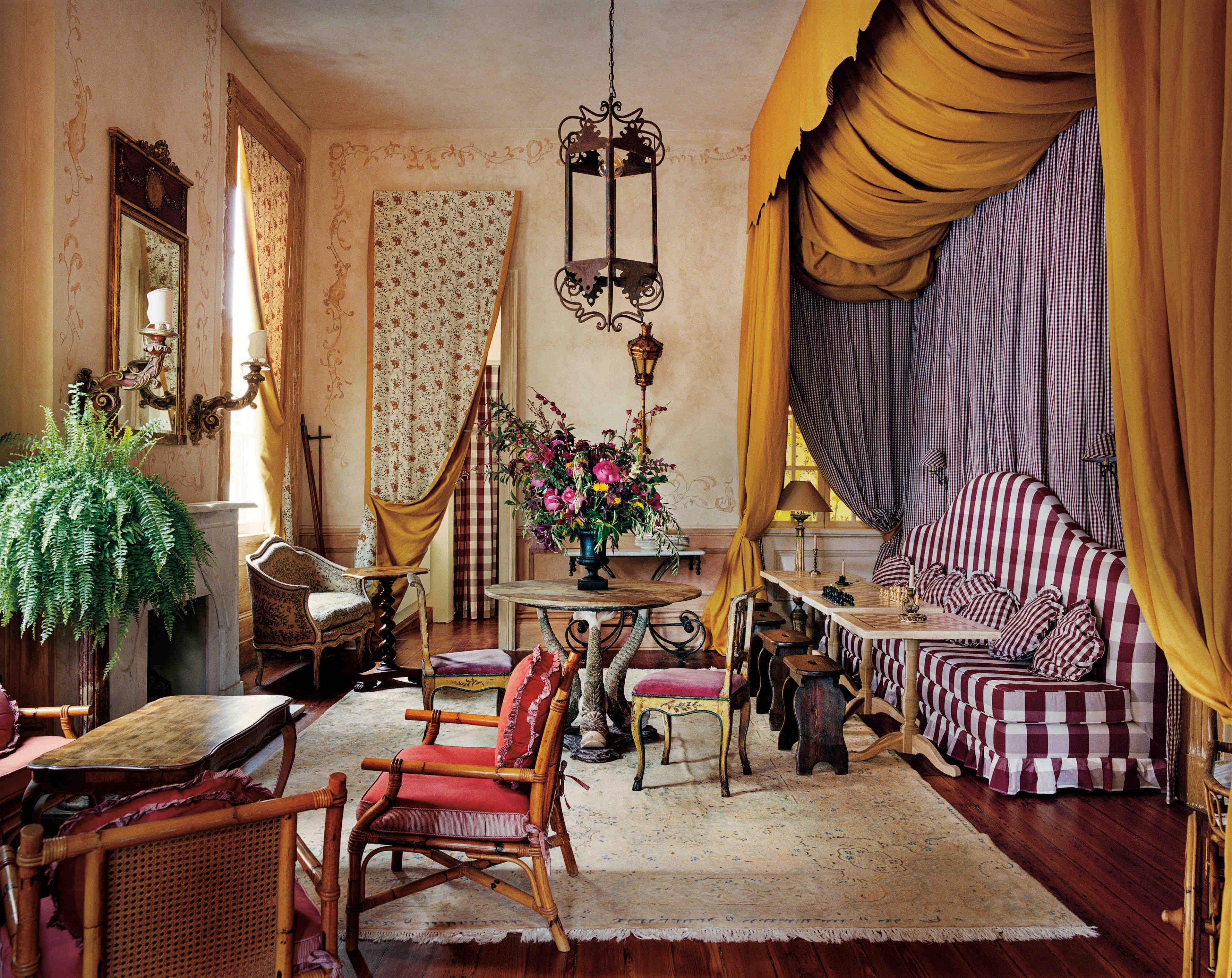 Ornate sitting room with gold drapes, checkered upholstery, antique chairs, plants, flowers, and a hanging lantern.