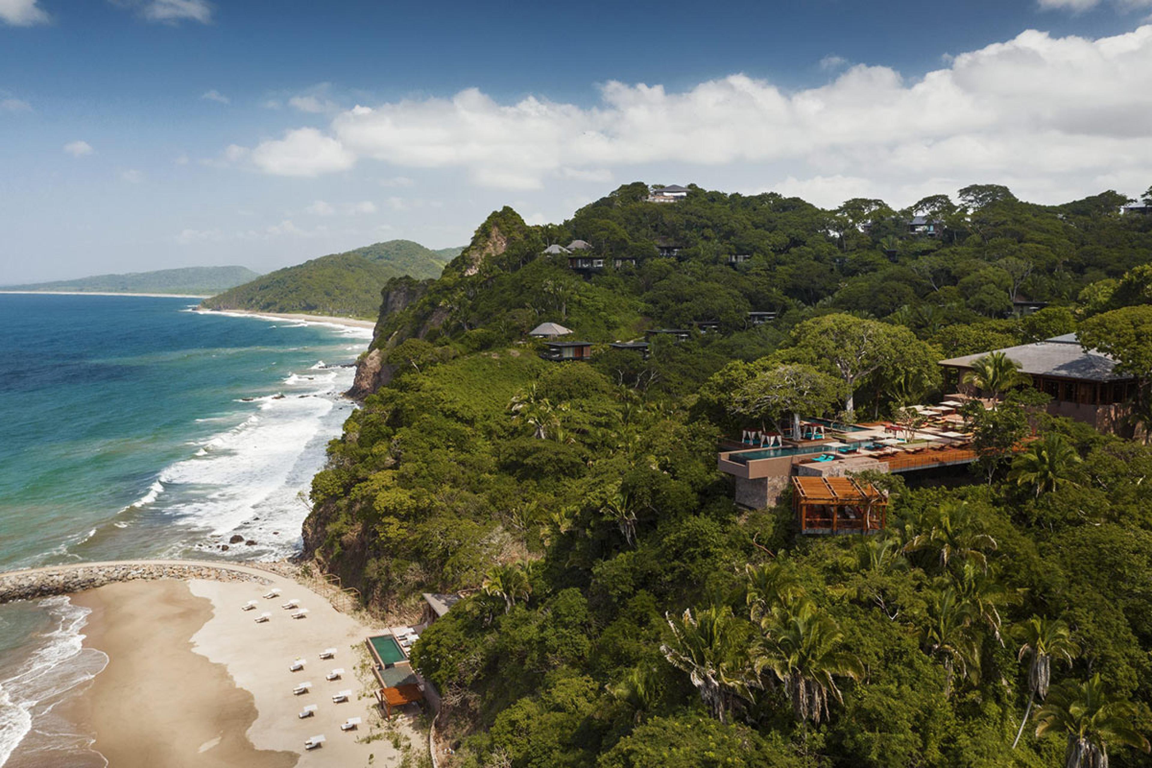 looking down a jungle coast with a hotel peeking through trees and two pools visible