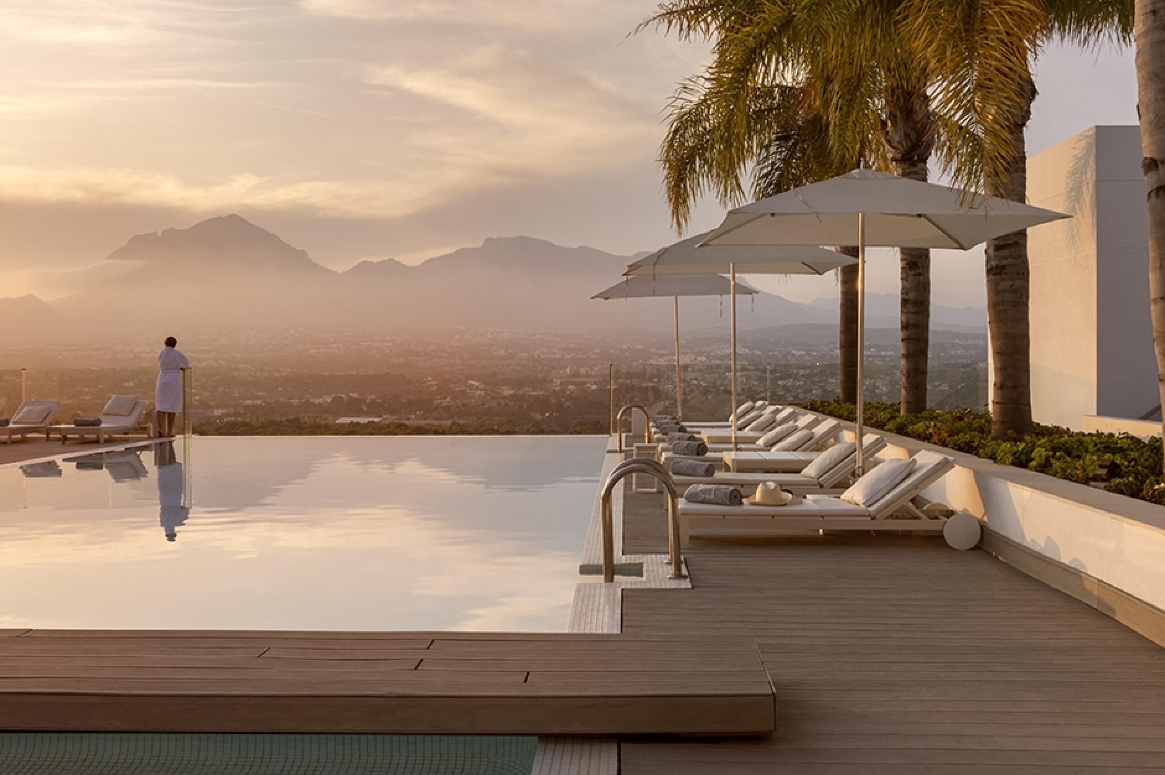 infinity pool with palm trees and mountains in background