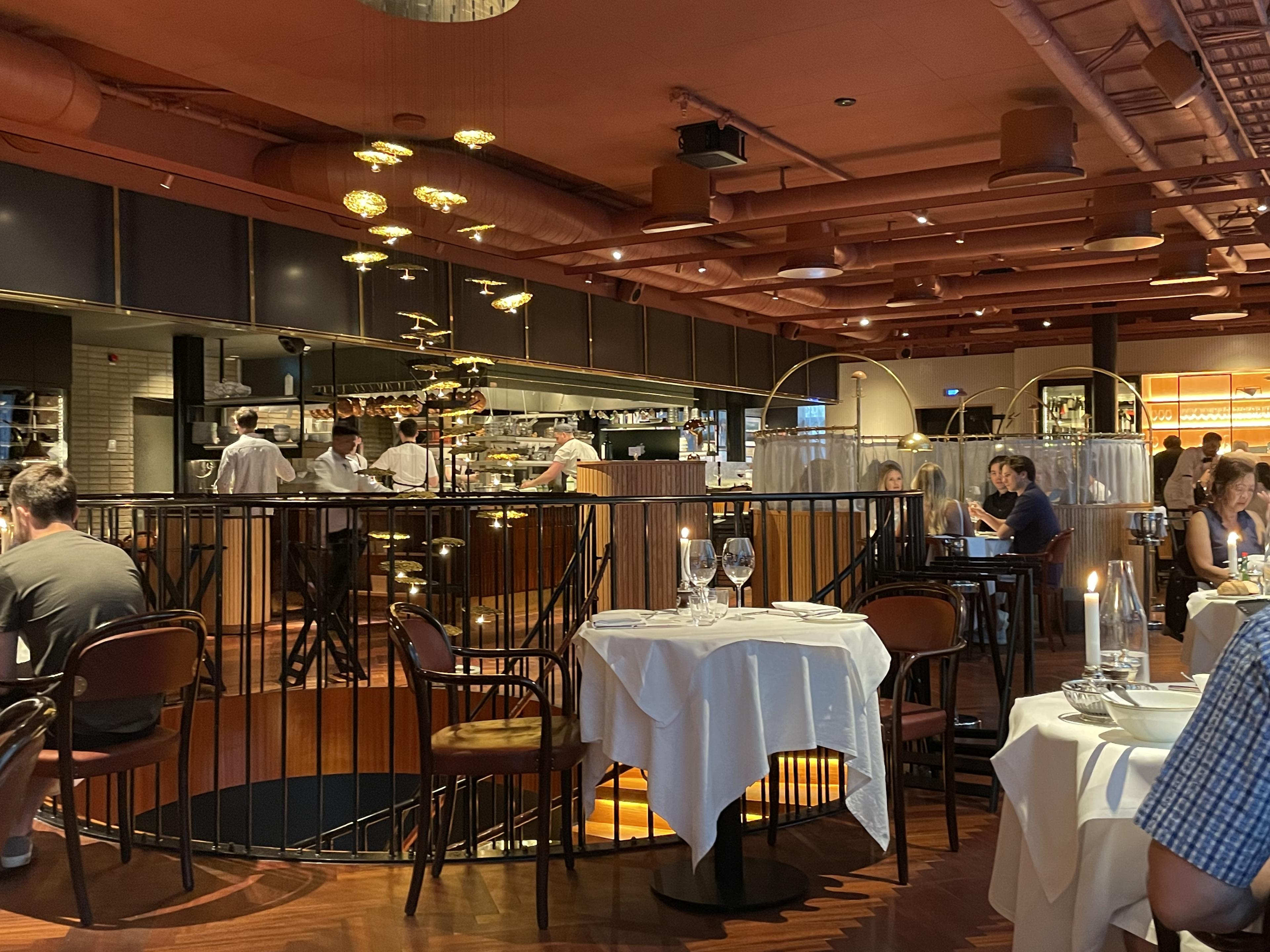 interior of warmly-lit restaurant with tables set for dinner and open kitchen in background