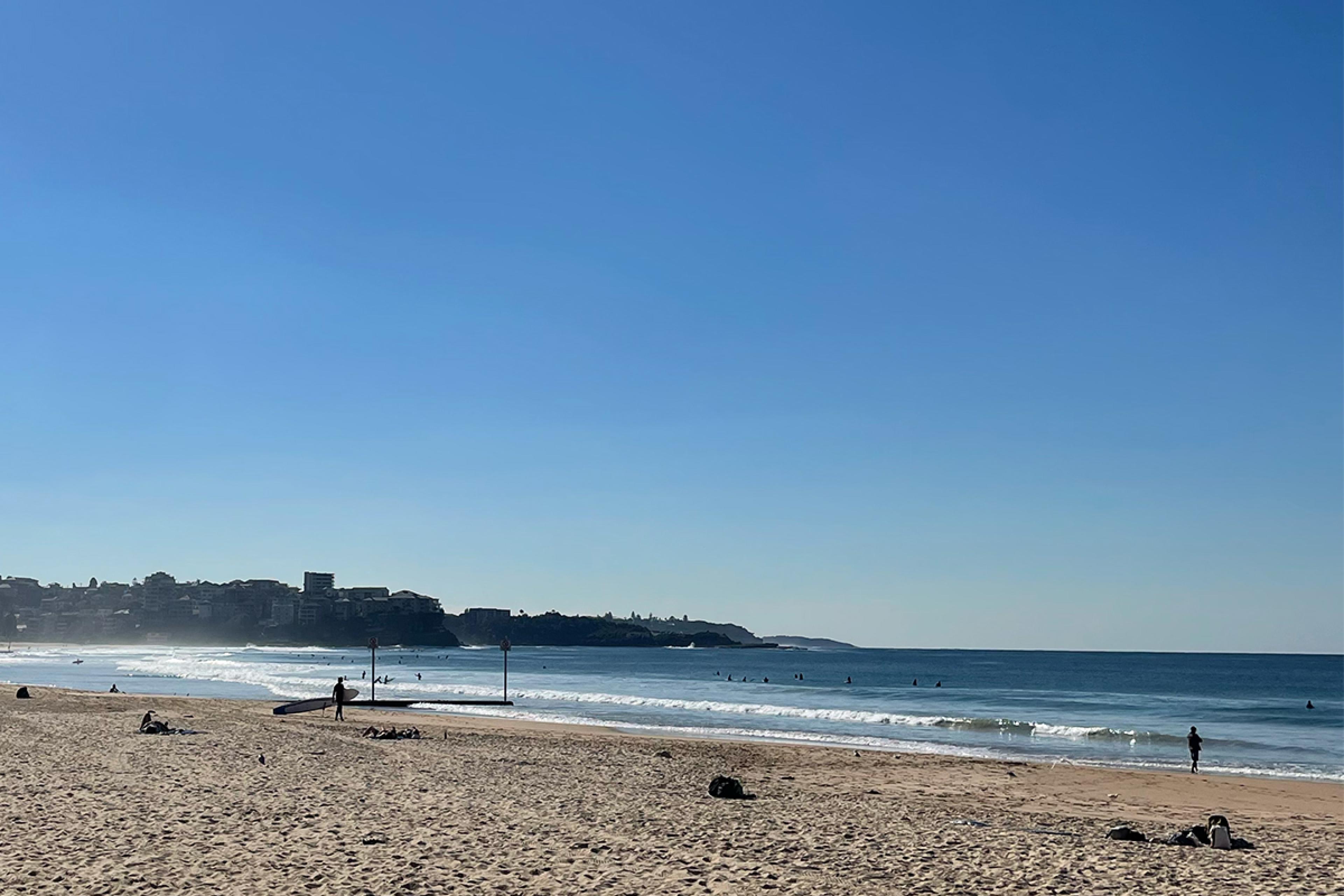 beach scene with person standing with surf board in background