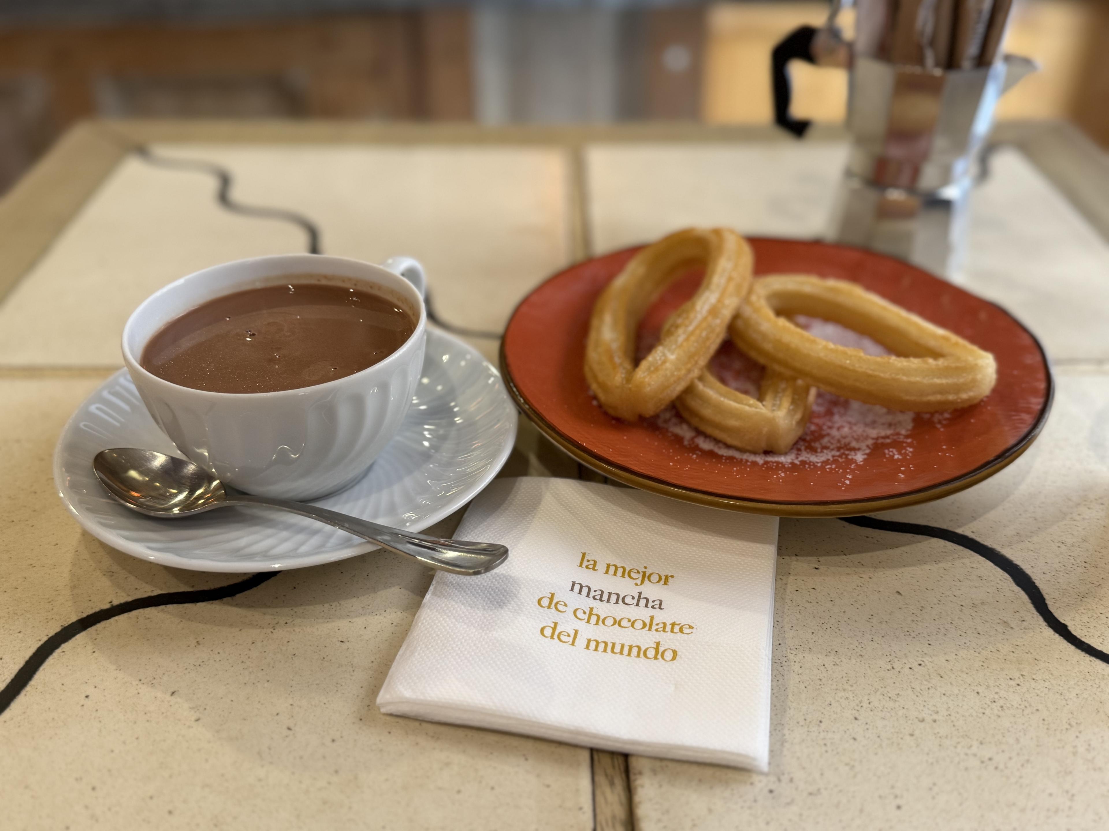 a cup of dipping chocolate next to a plate of churros