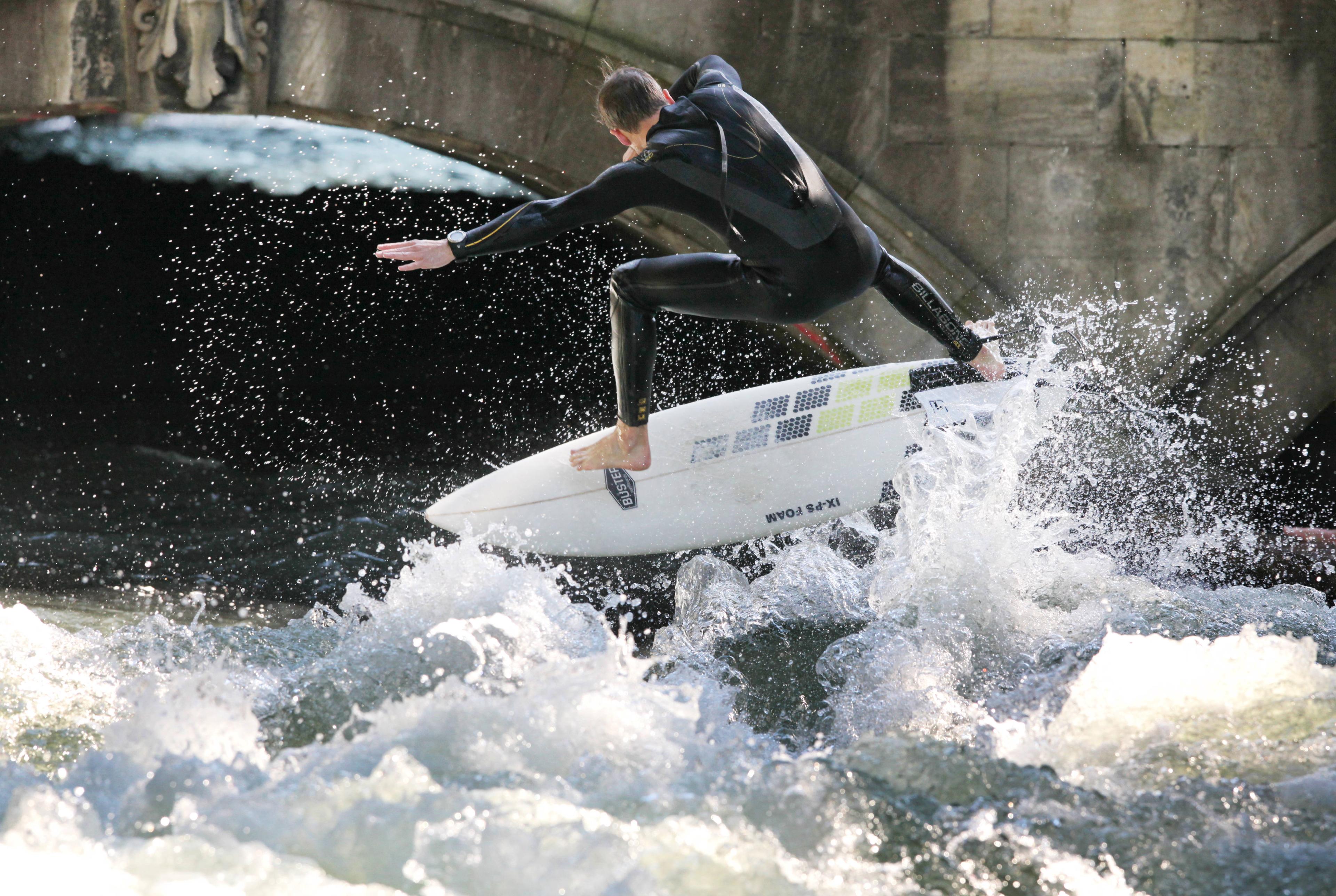 surfer in waves near a stone bridge